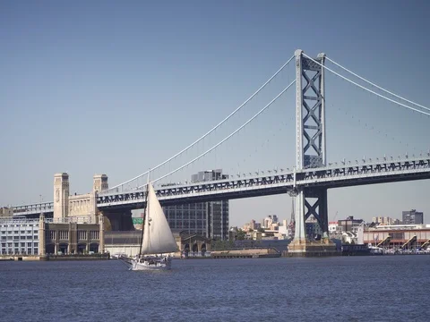 The ben franklin bridge with a sailboat on the delaware river, philadelphia Stock Footage 84901064