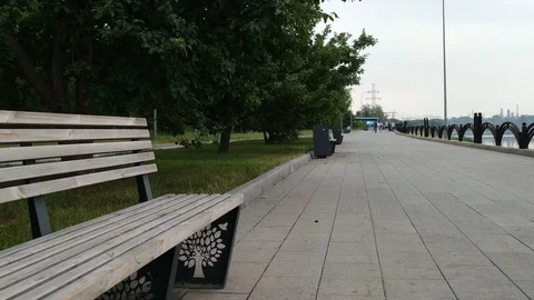 Bench in a city park along the river bank with condominiums Stock Footage
