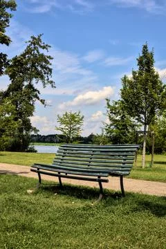 Bench by the edge of a path in a park next to a river on a clear day in summe Stock Photos
