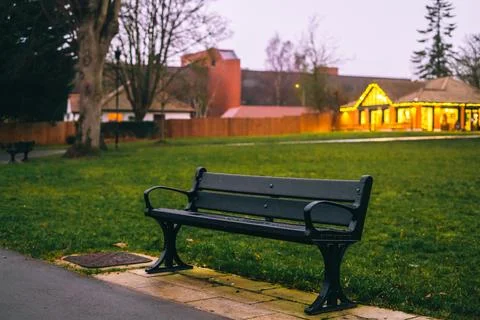 A bench in the foreground with an inviting café glows warmly in the dim light Foto stock