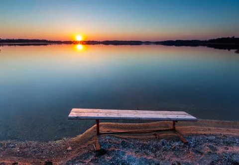 Bench on lake shore at sunset Stock Photos