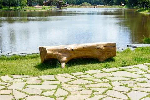 A bench made of a solid tree trunk on the bank of a pond. Stock Photos