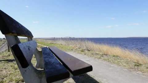 Bench on shore with cyclists passing by Stock Footage 22372782