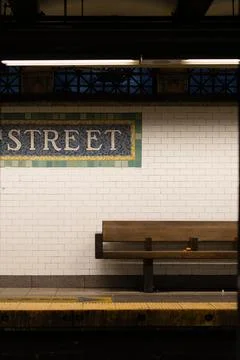 A bench is sitting in front of a white wall with a sign that says "Street" Stock Photos