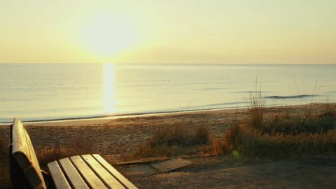 An bench standing on the seashore, against the background of the setting sun Stock Footage 303822283