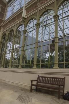 A bench stands next to the windows of a large glass, antique flower greenhouse 写真素材