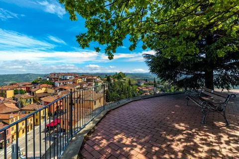 Bench under trees and view on small town in Piedmont, Italy. Stock Photos