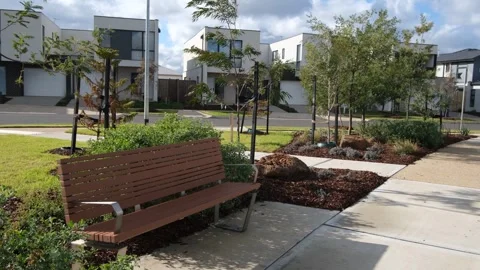 Bench, young trees, and low-maintenance plants in an Australian housing estate Vídeos de archivo 312423237