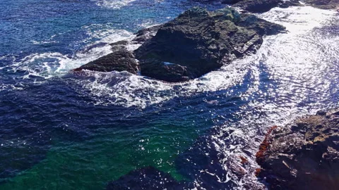 Beneath the bright sky, waves dance around rugged rocks along a tranquil coastal Stock Footage 332097050