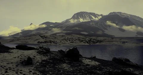 Beneath a twilight sky, towering mountains rise above tranquil waters 库存插图