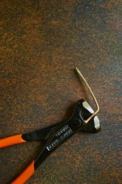 Bent old nail pulled out with a locksmiths pliers, forged metal, professional Stock Photos