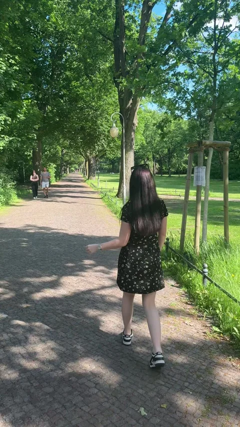Berlin, Germany - May 23, 2026 - young woman walks shaded park path, enjoying Stock Footage 336720460
