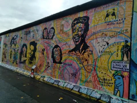 A Berlin Wall mural featuring faces of different people surrounded Stock Photos
