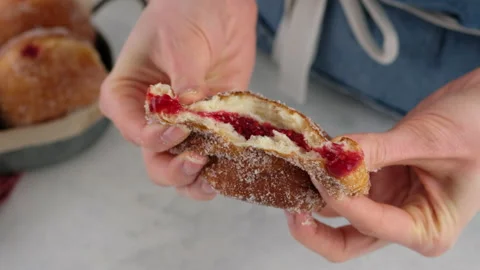 Berliners. Close-up female hands breaking a donut with raspberry jam on a white Stock Footage 146868120