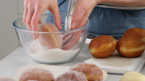 Berliners. Women's hands sprinkle sugar donuts in a glass bowl. Fried donuts in Video stock 146867072