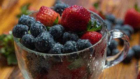 Berry pattern, red ripe strawberries and blueberry in a cup rotating on a wooden Stock Footage 275724558
