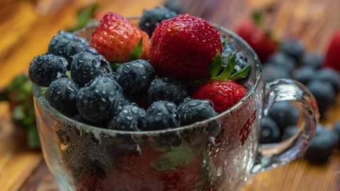 Berry pattern, red ripe strawberries and blueberry in a cup rotating on a wooden Stock Footage 276333925