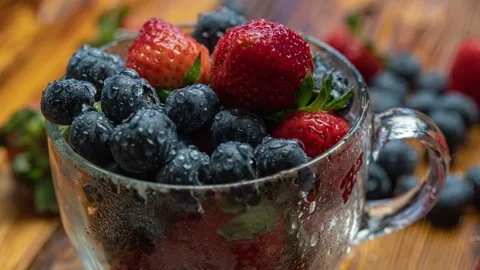 Berry pattern, red ripe strawberries and blueberry in a cup rotating on a wooden Stock Footage 276917349