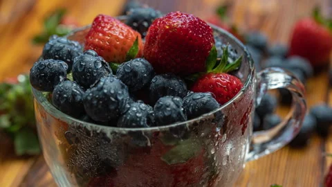 Berry pattern, red ripe strawberries and blueberry in a cup rotating on a wooden Stock Footage 277180288