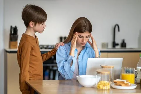 Besorgtes Kind Junge berührt Mutter sitzt am Küchentisch mit Laptop von Mü 스톡 사진