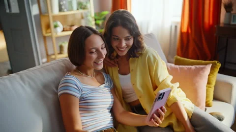 Besties video calling mobile phone sitting cozy couch closeup. Smiling couple Stock Footage 333320548