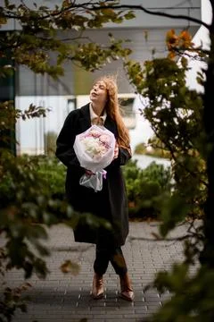 Between the branches of the trees stands a young woman with a delicate bouquet Stock Photos