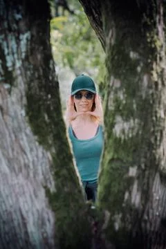 Between the forked trunks of a tree, a girl leaning her palms to her face Fotos Stock