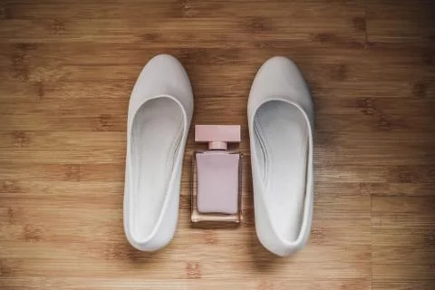 Between two white shoes are pink women's perfumes, eau de toilette. Stock Photos