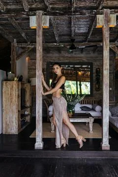 Between the wooden columns in the bungalow there is a girl in a top and a long Stock Photos