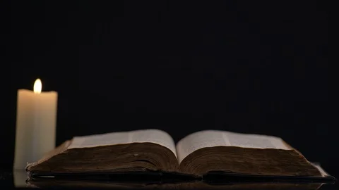 Bible and Wind Blowing Flame Of A Candle on Black Background 스톡 동영상 130154692