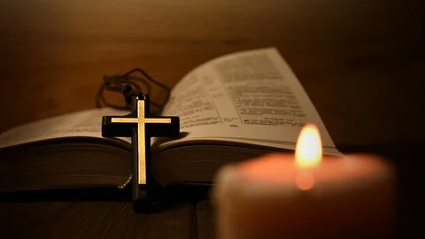 Bible is lying open on a table and a candle is burning Stock Footage 125928384