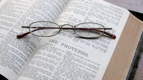 Bible open to the book of Proverbs, with a pair of reading glasses Vidéo 166631404