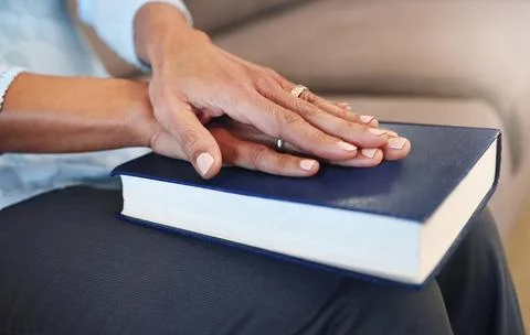 Bible, prayer and hands of old woman in living room for religion, book and Stock Photos