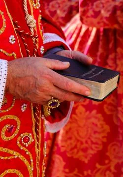 Bible with the sacred scriptures in the hands of the priest with red cassoc.. Stock Photos
