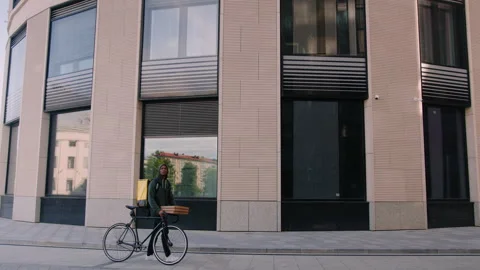 A bicycle courier with pizza boxes passes by a modern glass building Stock Footage 254098764