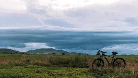 Bicycle in front of dark rain clouds hanging over the mountains Stock Photos