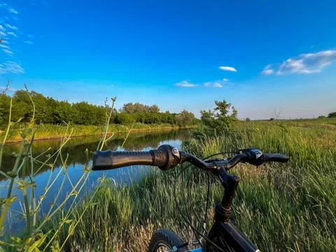 Bicycle handlebar overlooking tranquil river and lush greenery under blue sky Stock Photos