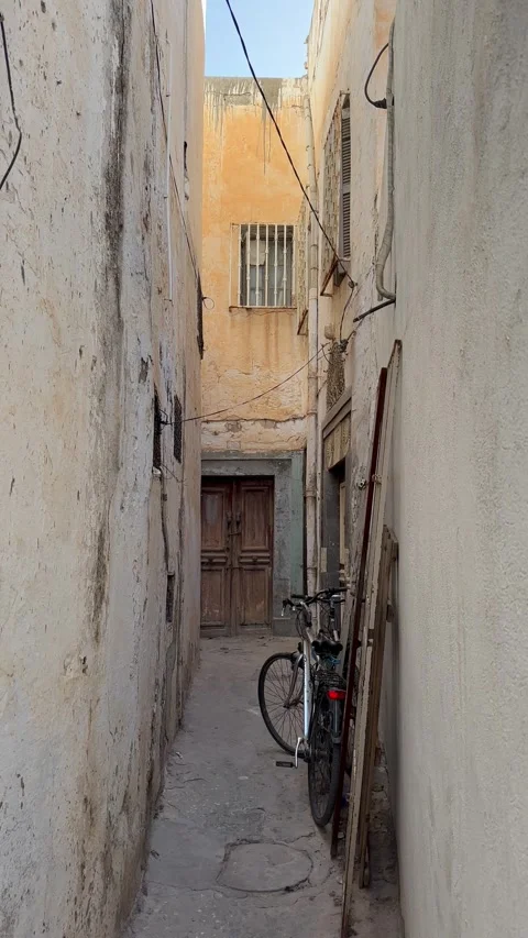 Bicycle leaning against a worn wall in a narrow sunlit alley between old Stock Footage 340959136