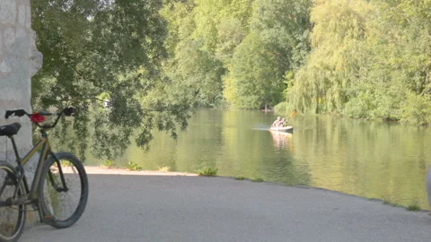 Bicycle parked by a stone wall along a scenic riverside path with a person kayak Stock-Footage 335694271