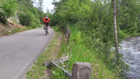 Bicycle rider riding away from camera down paved trail near creek/river 库存影片 339973935