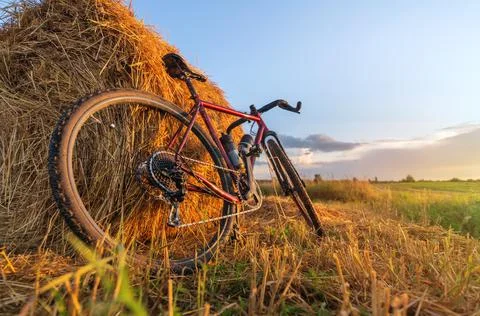 Bicycle stands by haystack in a field at sunset. Stock Photos