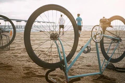 Bicycle upside down on the sand of the beach in the foreground with young peo Stock Photos
