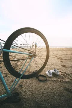 Bicycle upside down on the sand of the beach in the foreground with young peo Stock Photos