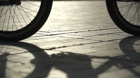 Bicycle wheels passing on the sidewalk in the evening, in front of the sun Stock Footage