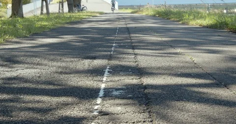 Bicycles pass the road. Mottled shadow of trees. Peaceful scene in summer. Stock Footage 120435415