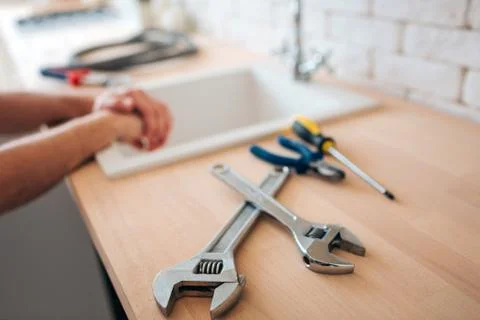 Big and small wrenches on table in kitchen. Screwdriver and nippers. Man's hands Stockfoto's