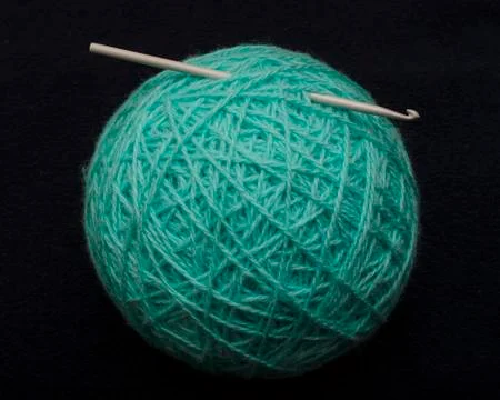 Big ball of turquoise acrylic-wool yarn on a dark background with a crochet h Stock Photos