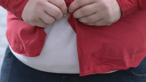 Big belly man buttoning up red shirt and pulling down, self-deception, dieting Stockbeeldmateriaal 89744601