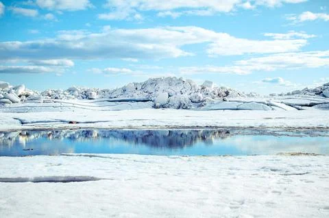 Big blocks of white ice and a puddle mirroring it on the shore of the bay on Stock Photos
