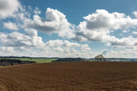 Big brown fields of fertile soil, green forest and wind power in the backgrou Stock Photos